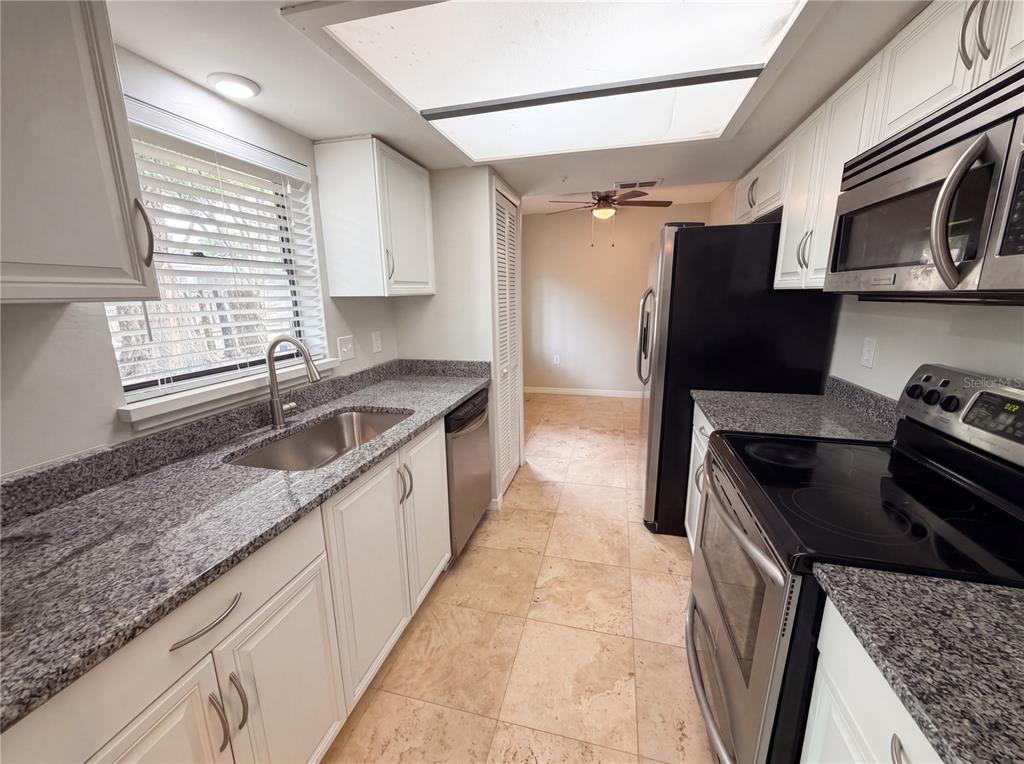 A galley kitchen features white cabinets, granite countertops, stainless steel appliances, and tile flooring — 3622 SHADY GROVE CIRCLE, ORLANDO, FL