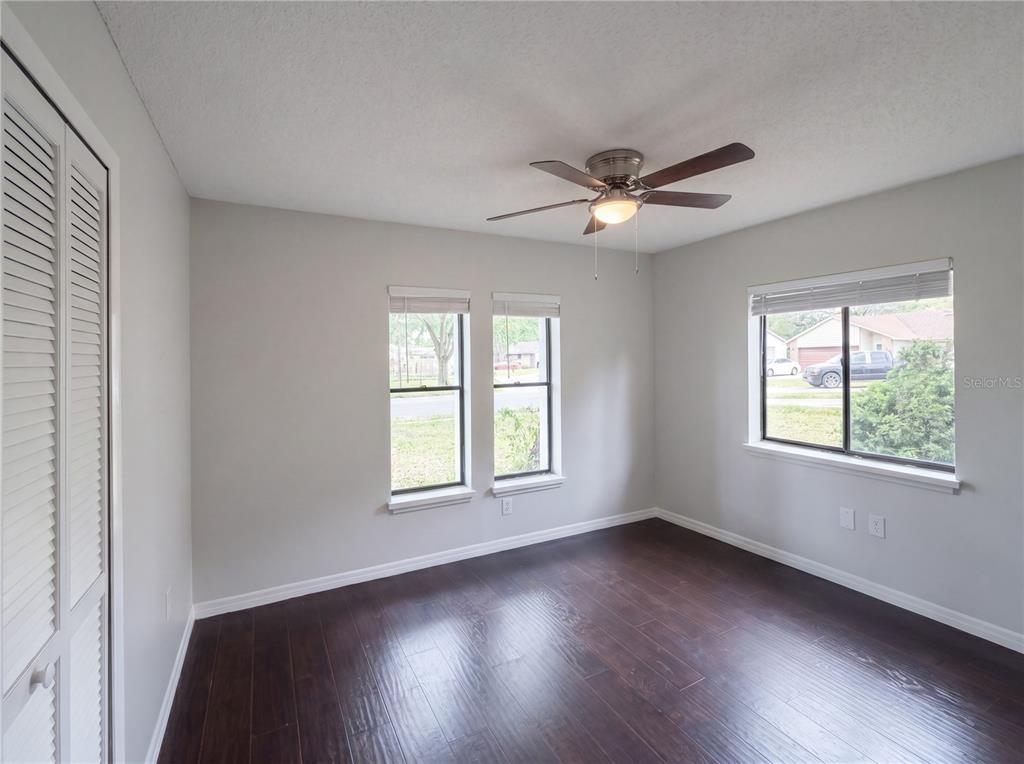 A bedroom with dark wood flooring, light gray walls, a ceiling fan, and three windows — 3622 SHADY GROVE CIRCLE, ORLANDO, FL