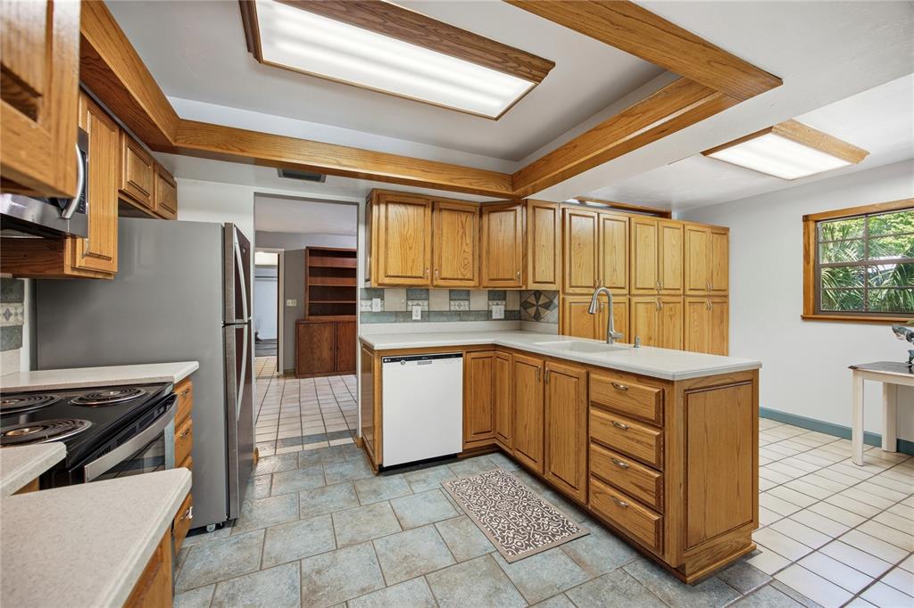 A kitchen with oak cabinets, a white dishwasher, a stainless refrigerator, and light tile flooring — 3519 NW 30TH BOULEVARD, GAINESVILLE, FL