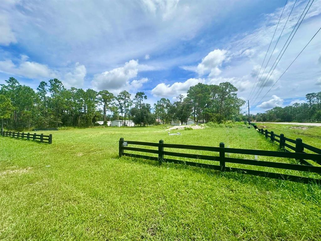 A grassy, fenced-in vacant lot is surrounded by trees under a blue, cloudy sky — 7218 BURKETT AVENUE, SEBRING, FL