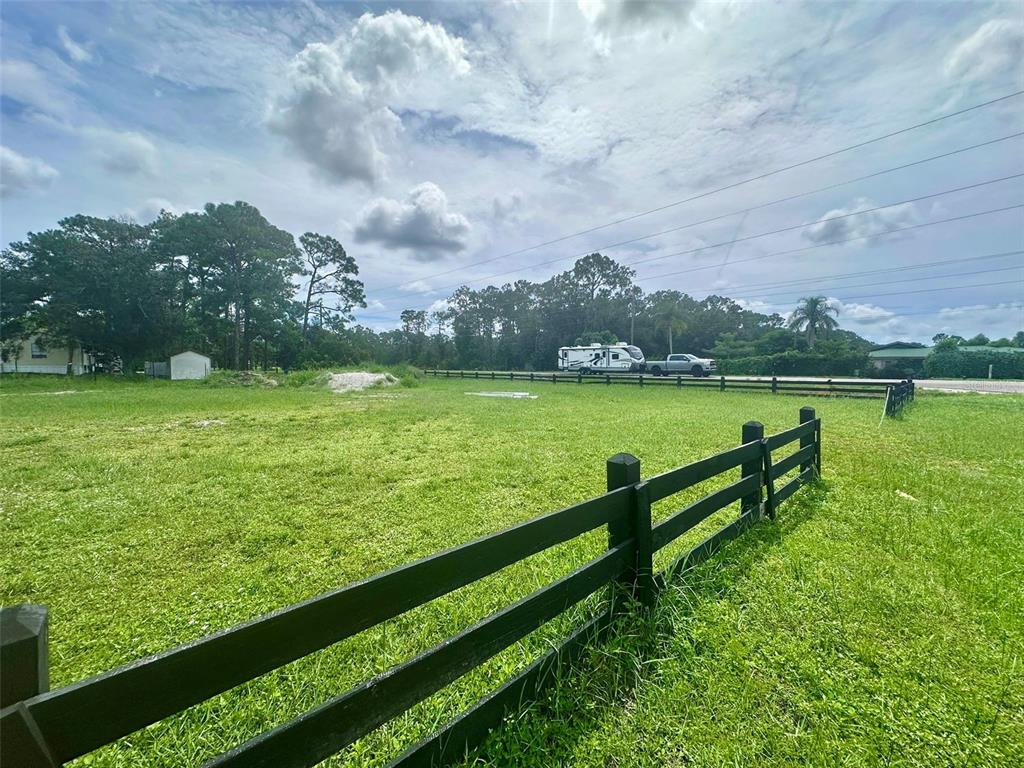A grassy, fenced-in vacant lot under a cloudy sky with trees in the background — 7218 BURKETT AVENUE, SEBRING, FL