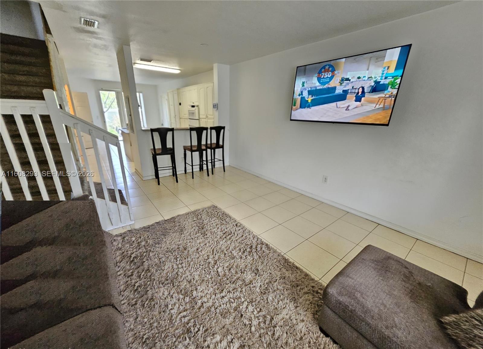 A living room with tile floors, a wall-mounted television, and stairs leading to an upper level — 3556 Oleander Ter # 3556, Riviera Beach FL 33404, RIVIERA BEACH, FL