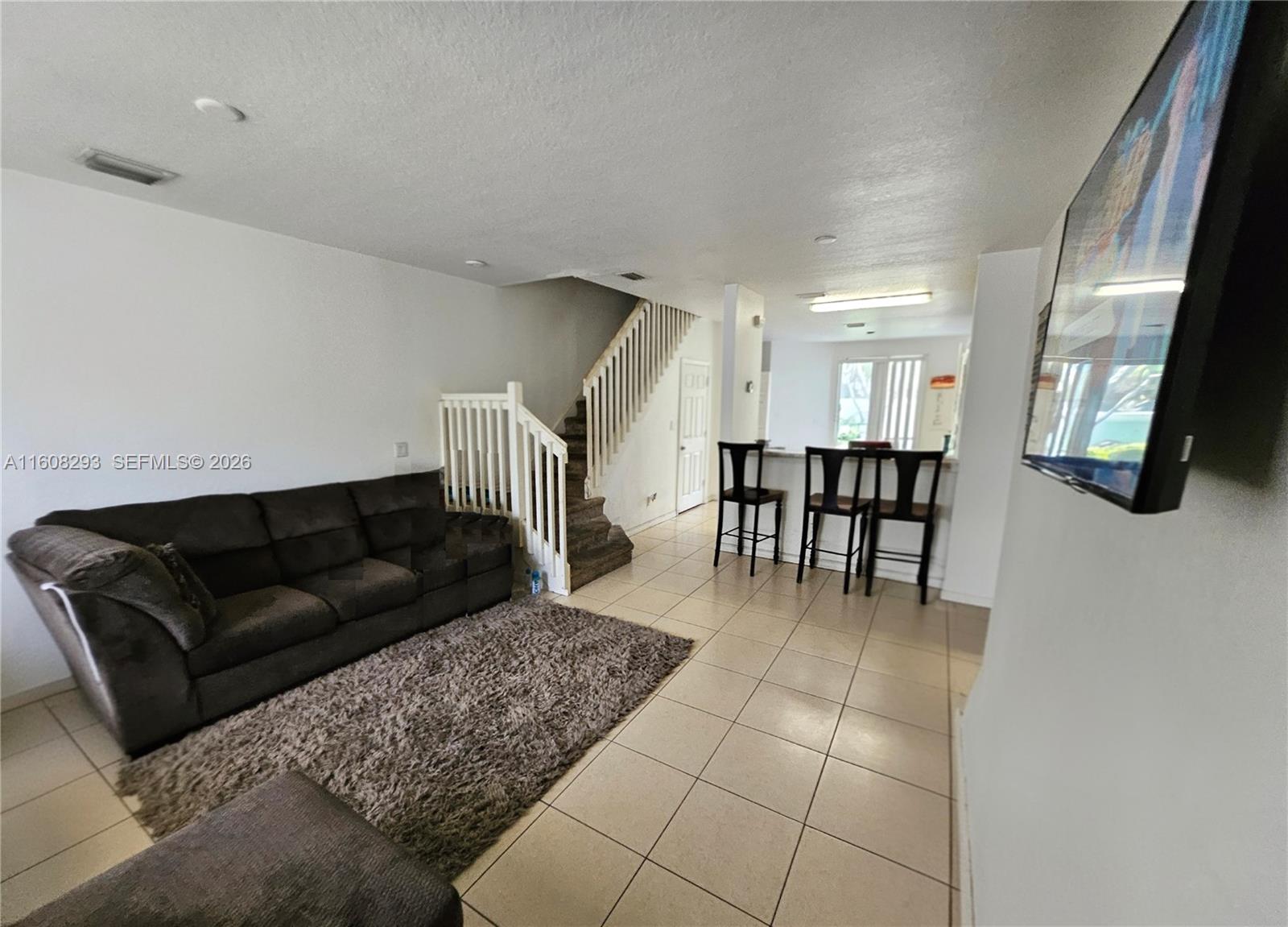 A living room features a dark sofa, a shaggy rug, tiled floors, and a staircase — 3556 Oleander Ter # 3556, Riviera Beach FL 33404, RIVIERA BEACH, FL