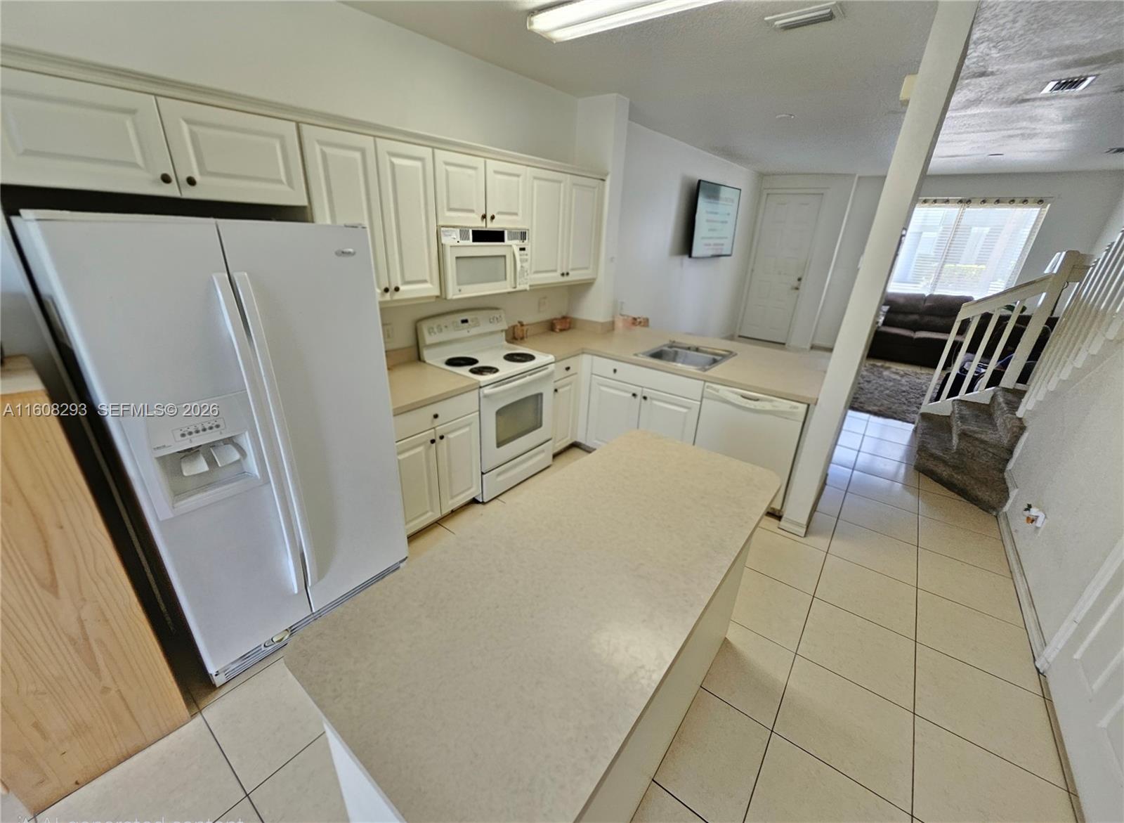 A kitchen features white cabinets, a central island, and light-colored tile flooring — 3556 Oleander Ter # 3556, Riviera Beach FL 33404, RIVIERA BEACH, FL
