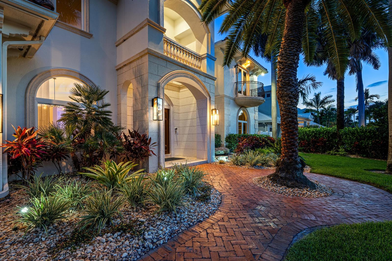 A brick walkway leads to the arched stone entrance of a two-story house at dusk — 2320 NE 34th Court, Lighthouse Point FL 33064, LIGHTHOUSE POINT, FL