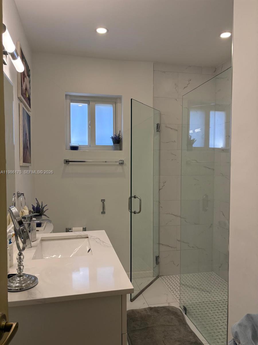 A bathroom features a white vanity, a glass-enclosed shower with marble-look tiles, and a window — 1758 SW 18th St, Miami FL 33145, MIAMI, FL