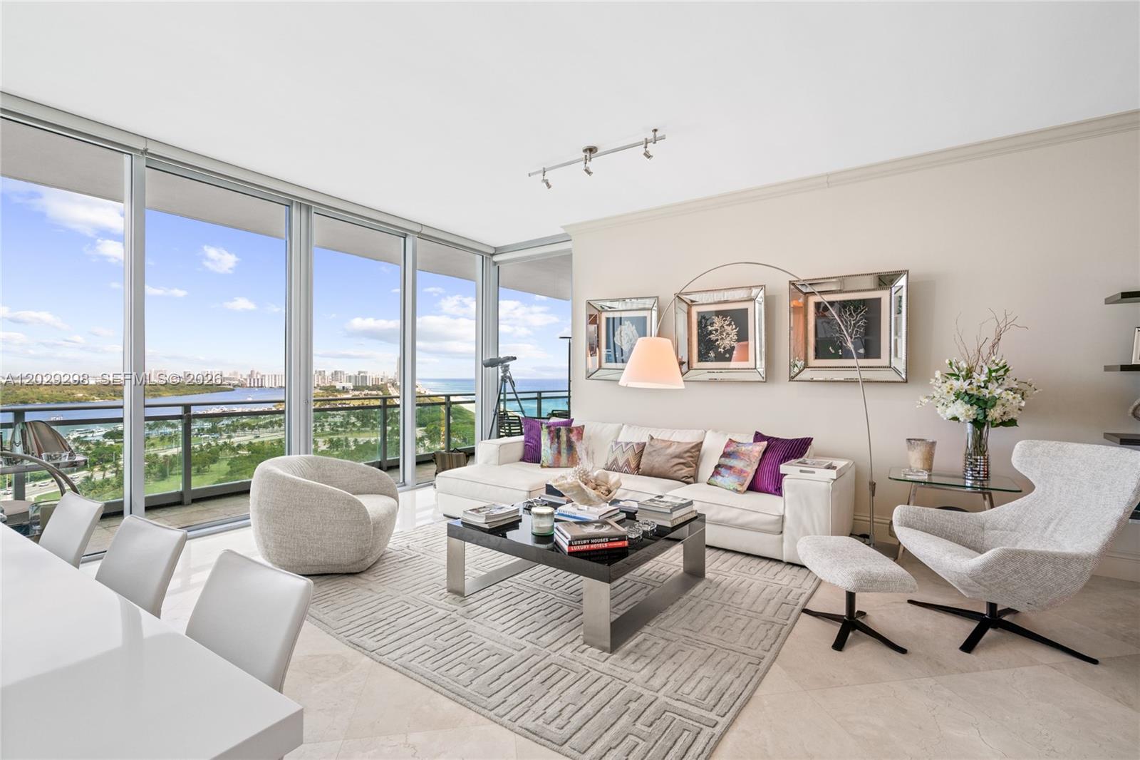 A modern living room features a white sofa, patterned rug, and floor-to-ceiling windows with ocean views — 10295 Collins Ave # 1606, Bal Harbour FL 33154, BAL HARBOUR, FL