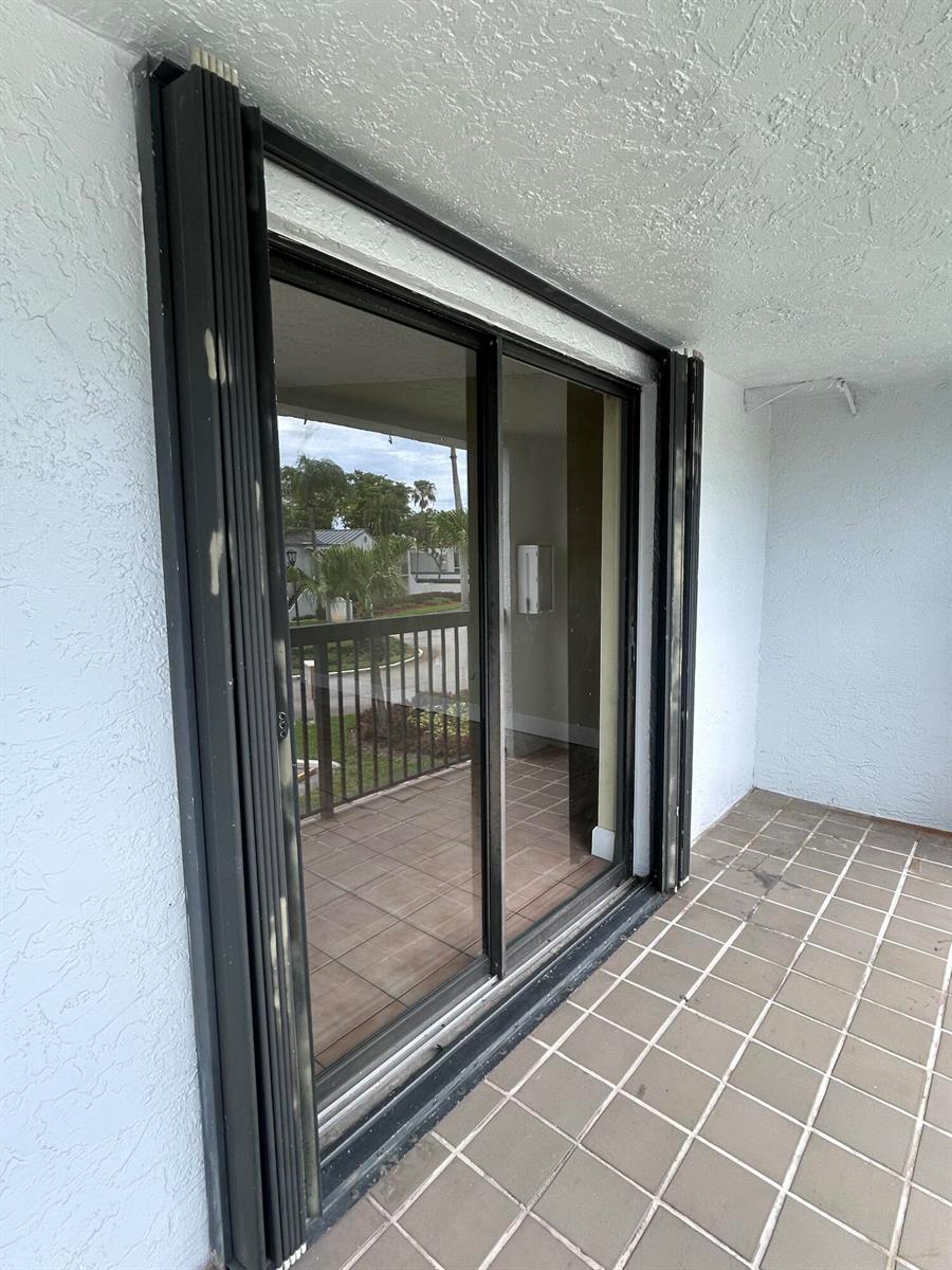 A sliding glass door with black accordion-style hurricane shutters installed on a tiled balcony — 18310 Mediterranean Boulevard # 24, Hialeah FL 33015, HIALEAH, FL