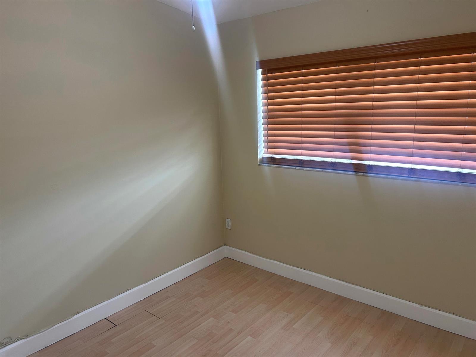 An empty room with light-colored walls, wood-look flooring, white baseboards, and a window with blinds — 18310 Mediterranean Boulevard # 24, Hialeah FL 33015, HIALEAH, FL