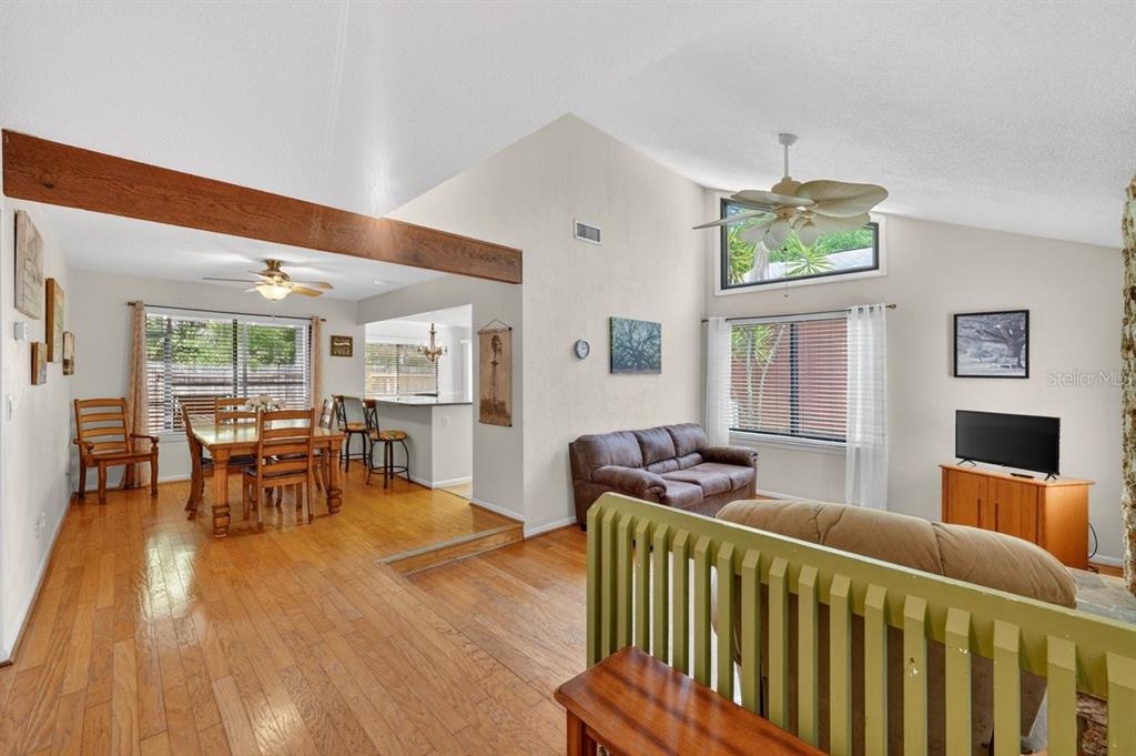 An open-concept living and dining area with hardwood floors, vaulted ceilings, and a wooden beam — 302 GATEWOOD COURT, ORMOND BEACH, FL