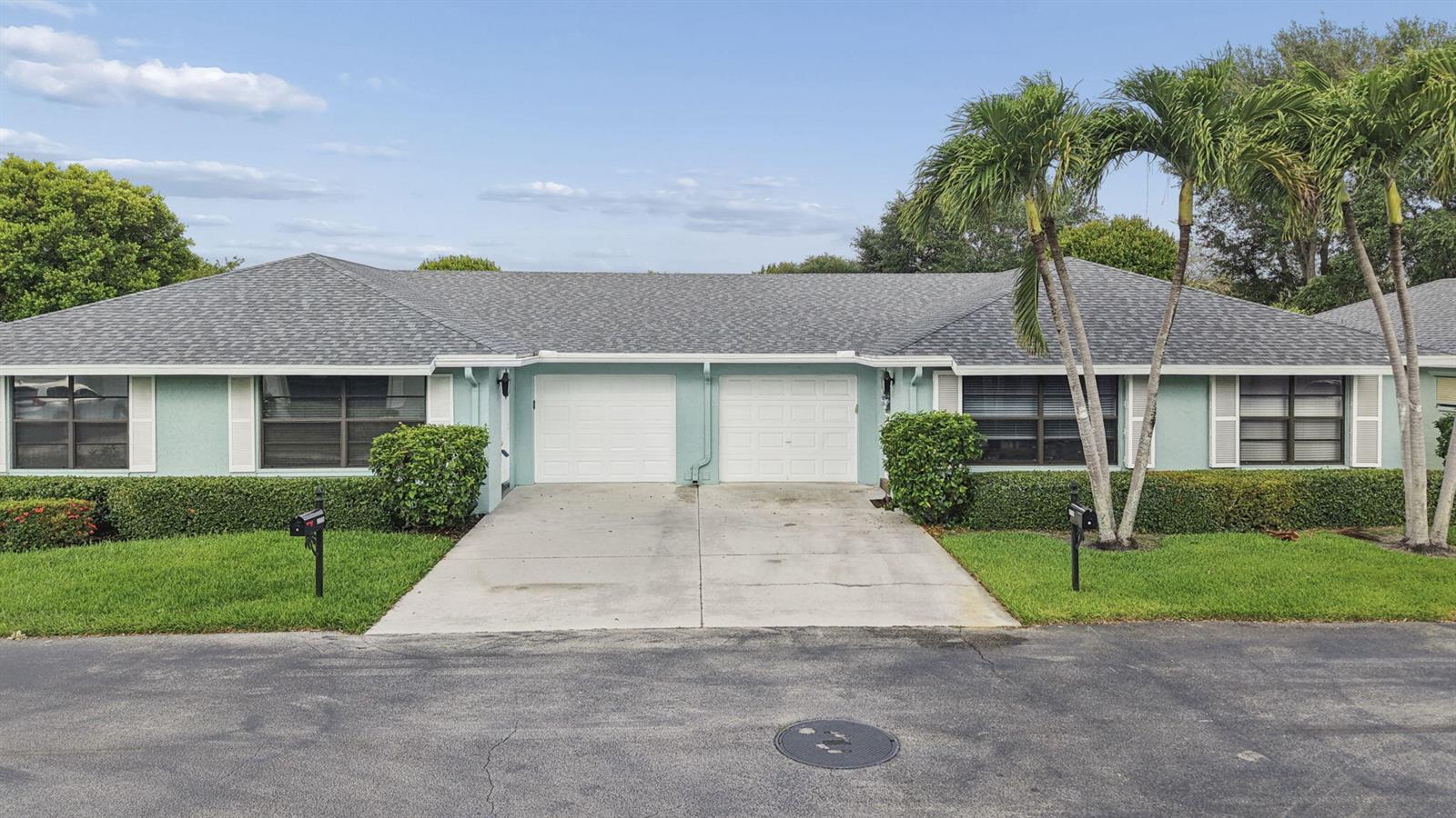 A single-story duplex with light blue siding, two garage doors, and a shared driveway — 9860 Pecan Tree Drive # A, Boynton Beach FL 33436, BOYNTON BEACH, FL