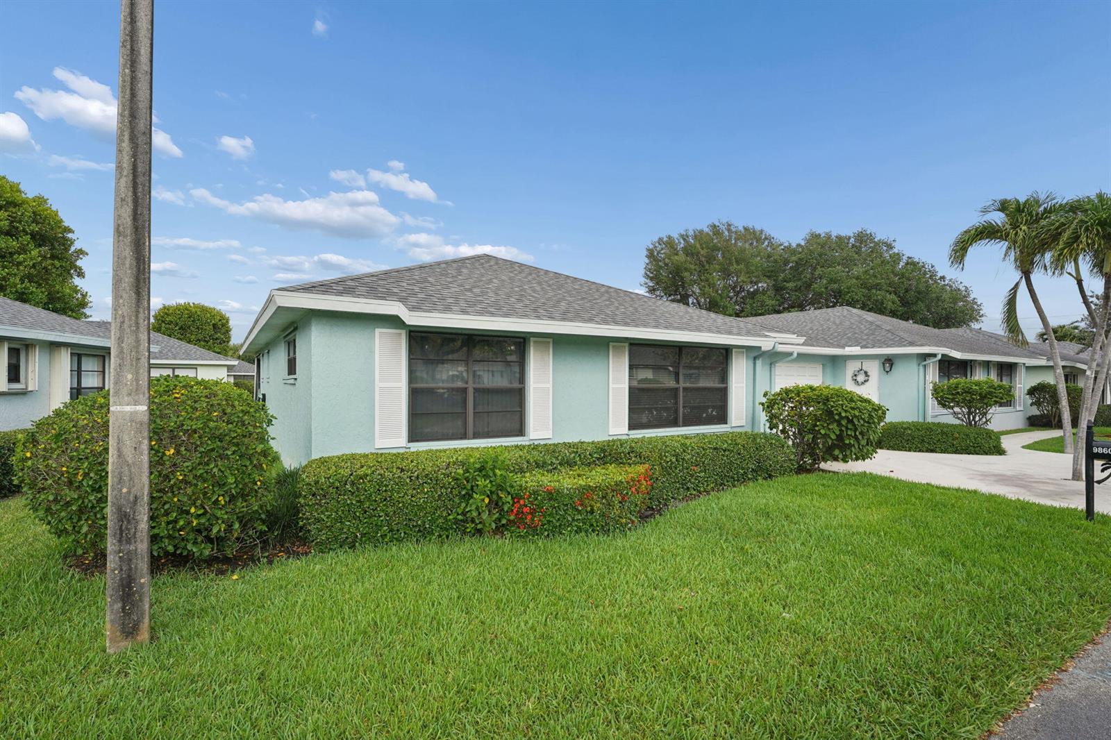 A light blue, single-story house with a shingled roof and manicured hedges in the front — 9860 Pecan Tree Drive # A, Boynton Beach FL 33436, BOYNTON BEACH, FL