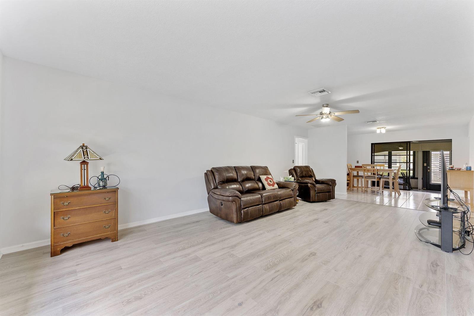 A living room features light wood-look flooring, a brown leather sofa, and a wooden dresser — 9860 Pecan Tree Drive # A, Boynton Beach FL 33436, BOYNTON BEACH, FL