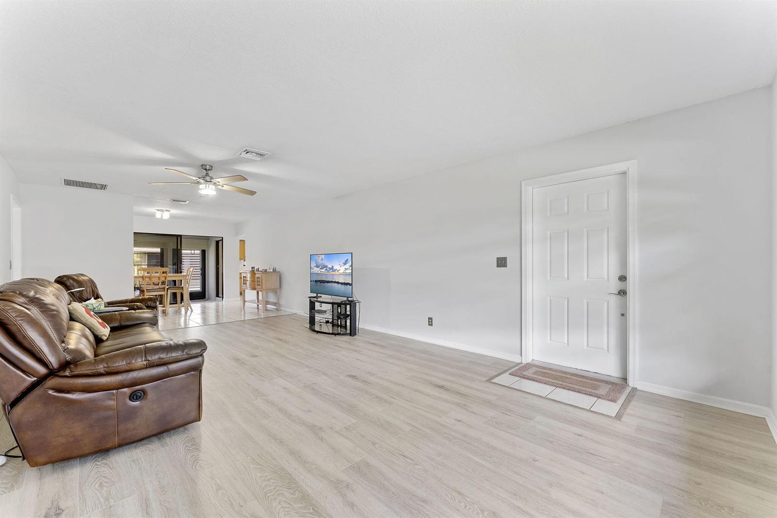 A living room features light wood-look flooring, a brown leather sofa, and a front door — 9860 Pecan Tree Drive # A, Boynton Beach FL 33436, BOYNTON BEACH, FL