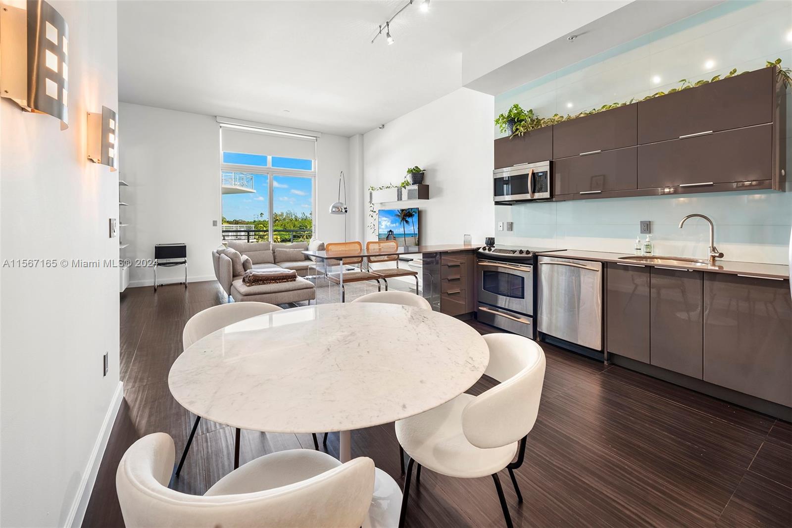 A modern open-plan kitchen and dining area features dark cabinetry, marble tables, and large windows — 2001 Meridian Ave # 517, Miami Beach FL 33139, MIAMI BEACH, FL