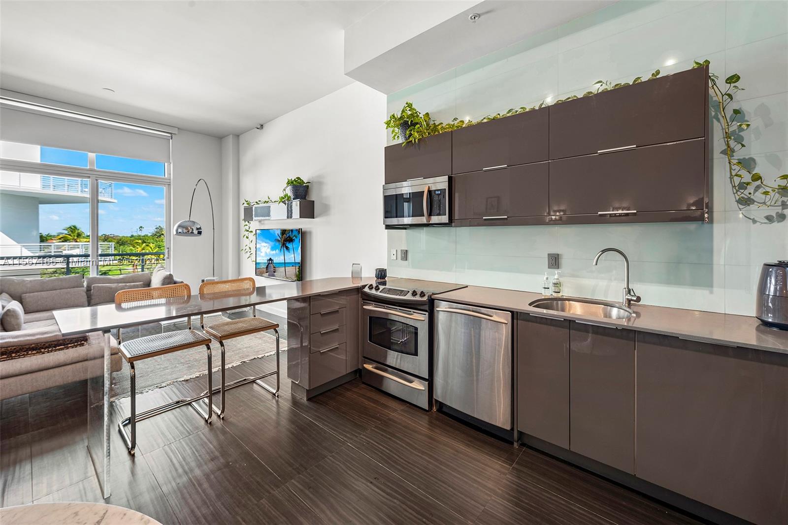 A modern kitchen with dark cabinetry and stainless steel appliances opens into a living area — 2001 Meridian Ave # 517, Miami Beach FL 33139, MIAMI BEACH, FL