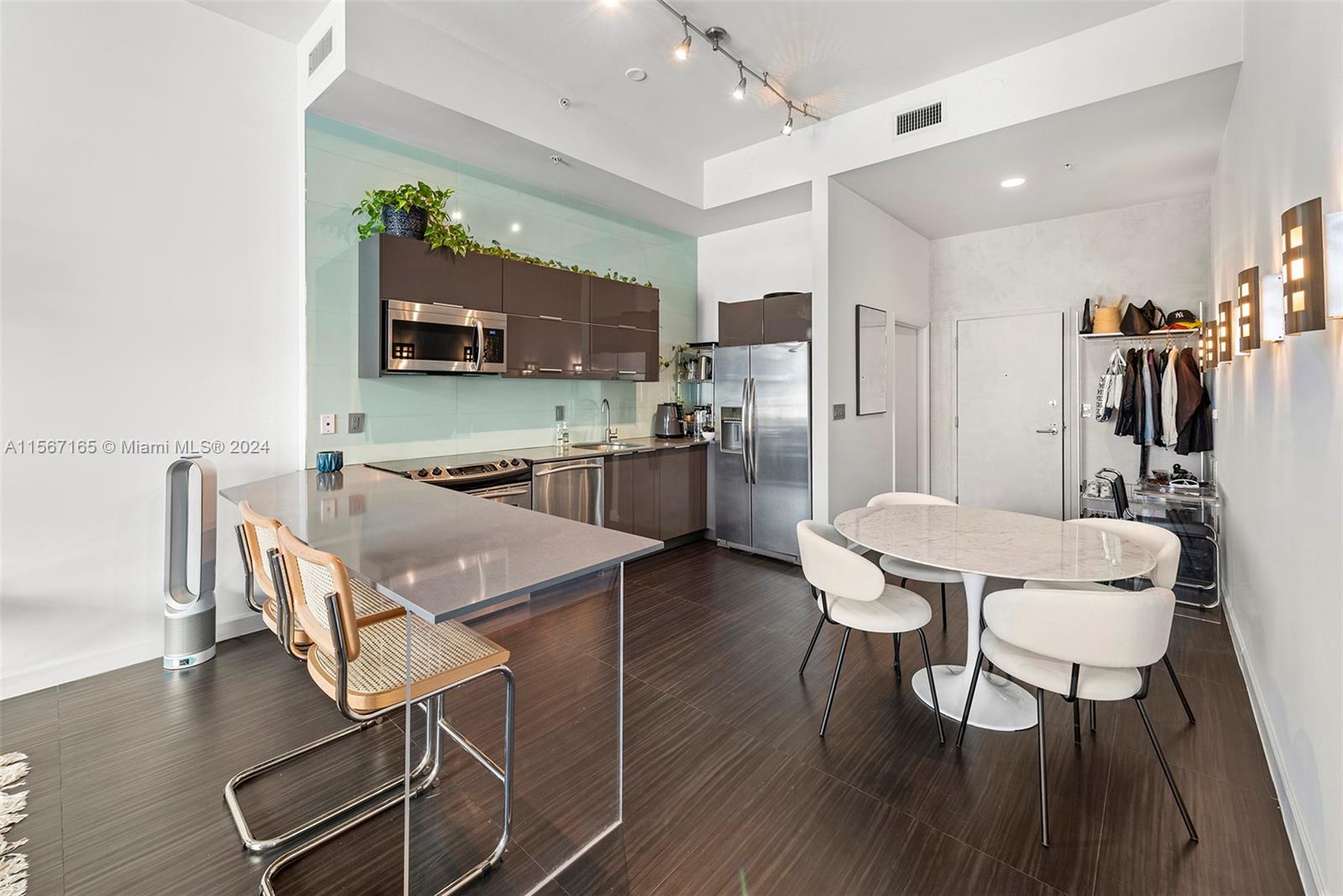 A modern kitchen features dark cabinetry, stainless steel appliances, a breakfast bar, and dining area — 2001 Meridian Ave # 517, Miami Beach FL 33139, MIAMI BEACH, FL