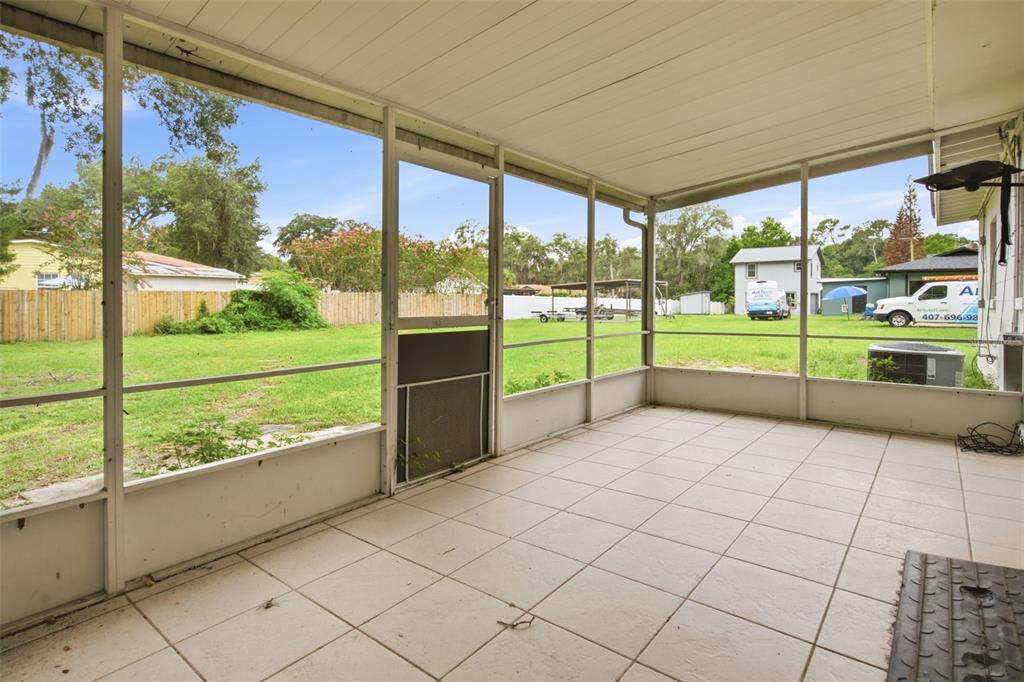 A screened-in porch with white tile flooring overlooks a grassy backyard with a fence — 452 OAKHURST STREET, ALTAMONTE SPRINGS, FL