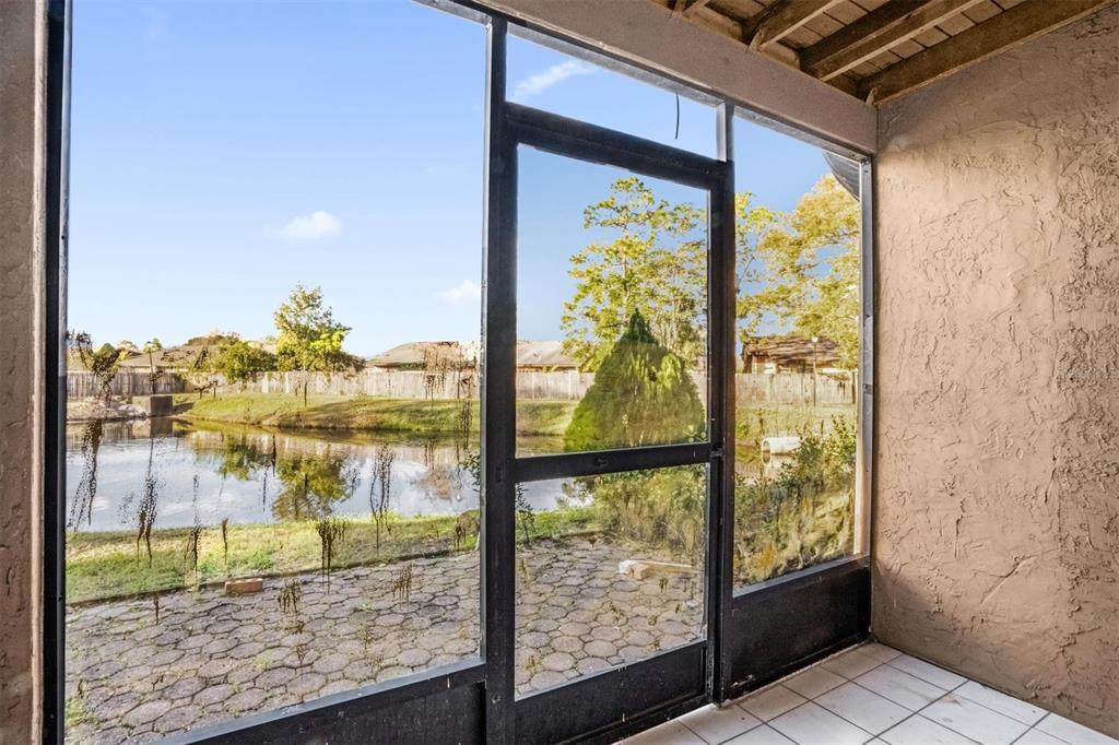 A screened-in patio with tiled flooring overlooks a small pond and a residential backyard — 1822 FOXHALL CIRCLE UNIT 1822, KISSIMMEE, FL
