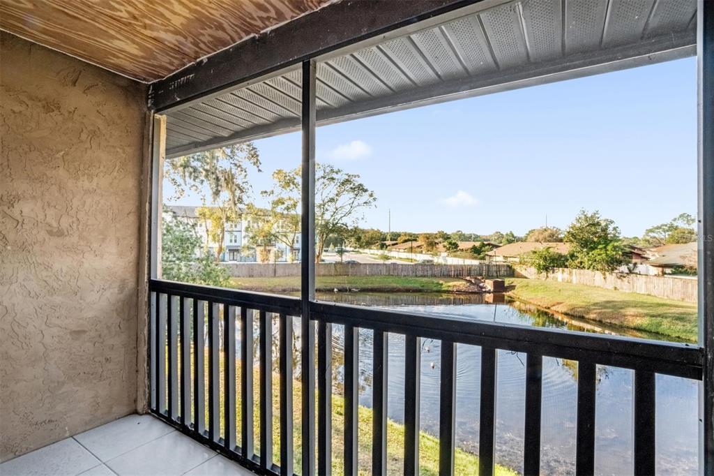 A screened-in balcony with tile flooring overlooks a small pond and a wooden fence — 1822 FOXHALL CIRCLE UNIT 1822, KISSIMMEE, FL