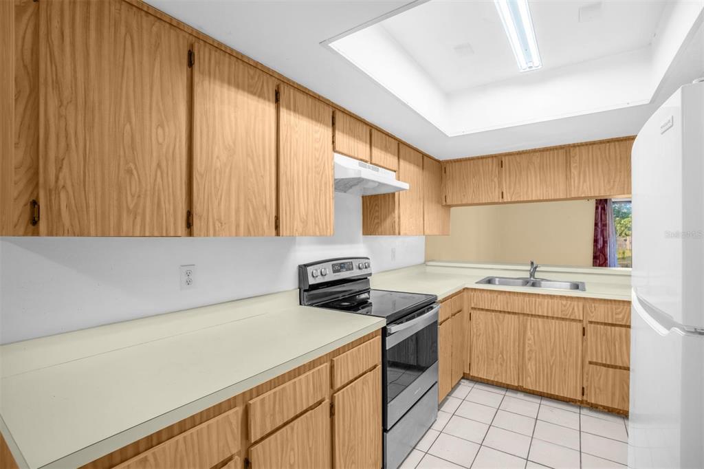 A kitchen features light wood cabinets, white countertops, a white stove, and a tiled floor — 1822 FOXHALL CIRCLE UNIT 1822, KISSIMMEE, FL