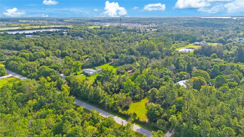 An aerial view shows a house surrounded by dense trees, green lawns, and a road — 0 HENRY J AVENUE, ST CLOUD, FL