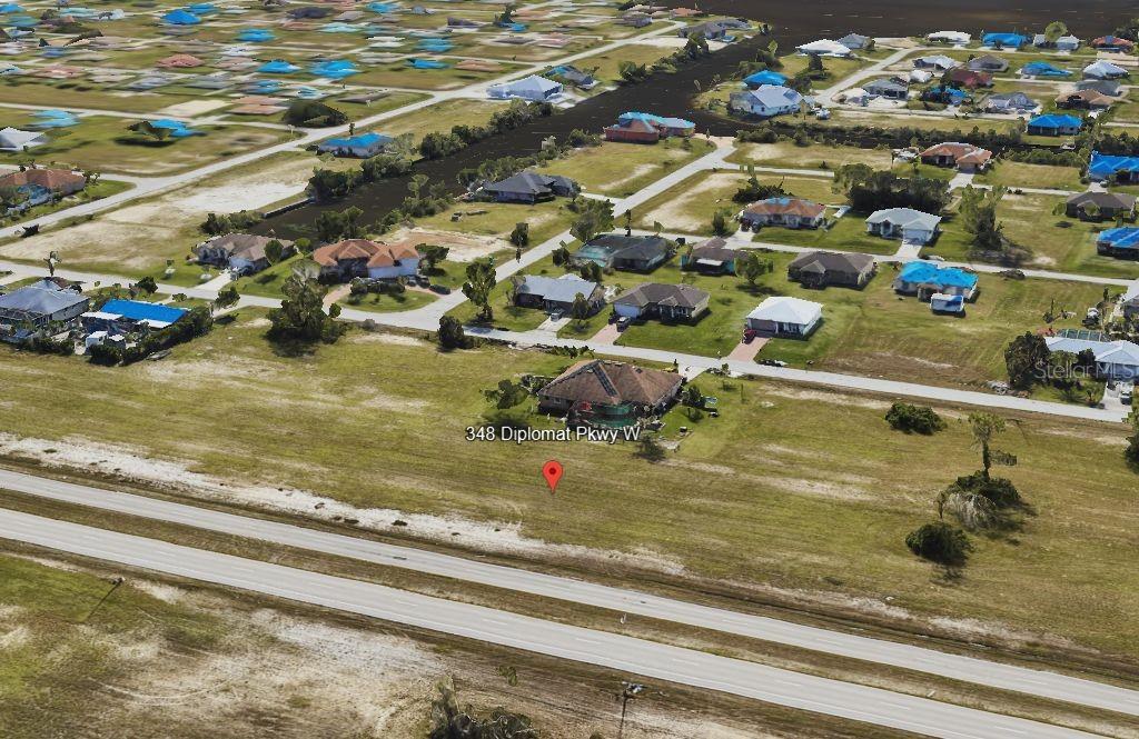 An aerial view shows a residential house with a brown roof surrounded by grassy lots — 348 DIPLOMAT PARKWAY W, CAPE CORAL, FL