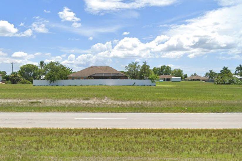 A vacant grassy lot sits in front of a white fence and a residential house — 348 DIPLOMAT PARKWAY W, CAPE CORAL, FL