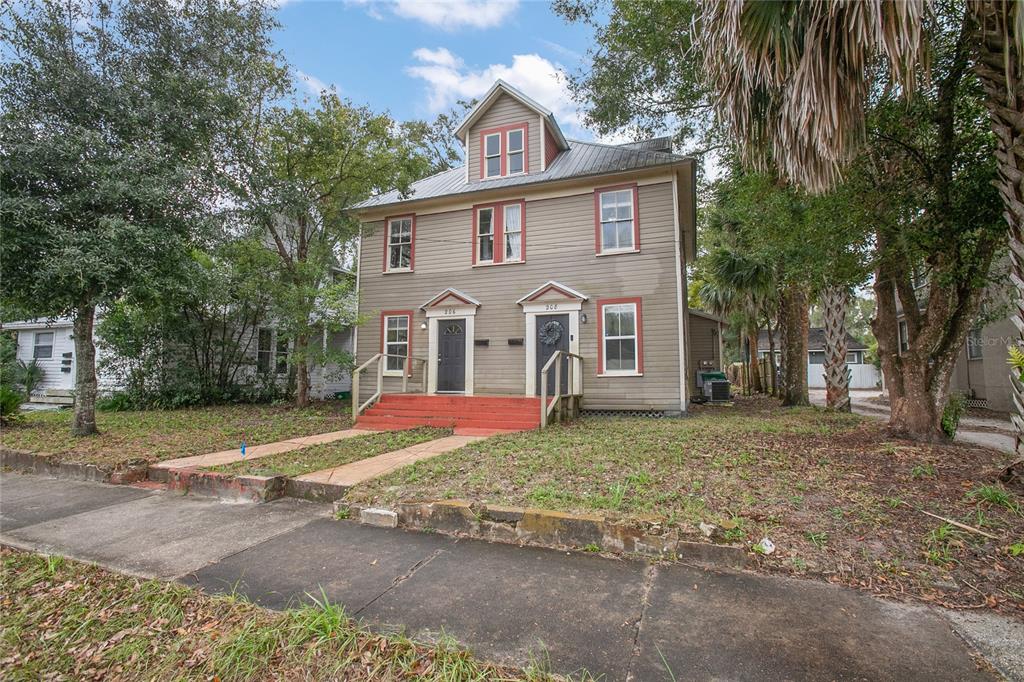 A two-story duplex with gray siding, red trim, and a metal roof sits on a lot — 206 W WISCONSIN AVENUE, DELAND, FL