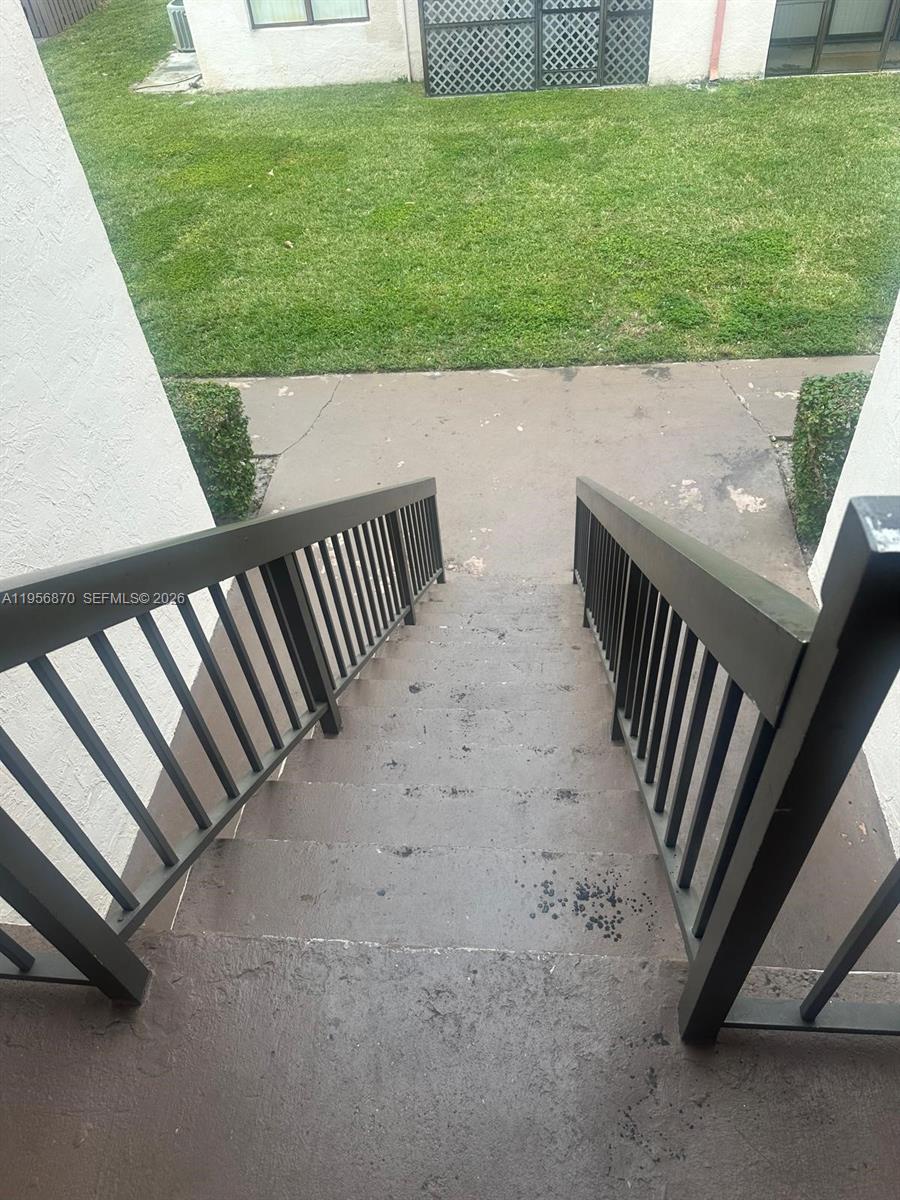 An outdoor staircase with dark railings leads down to a concrete patio and lawn — 855 NE 209th St # 34, Miami FL 33179, MIAMI, FL