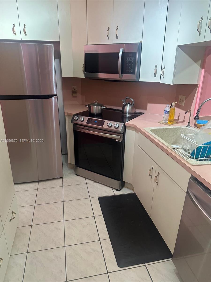 A kitchen features stainless steel appliances, light-colored cabinetry, pink countertops, and tiled flooring — 855 NE 209th St # 34, Miami FL 33179, MIAMI, FL