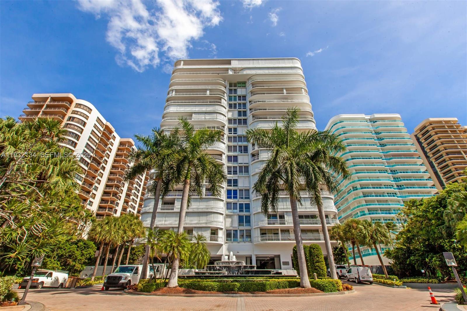 A low-angle view of a white high-rise residential building with balconies and palm trees — 10155 Collins Ave # 410, Bal Harbour FL 33154, BAL HARBOUR, FL