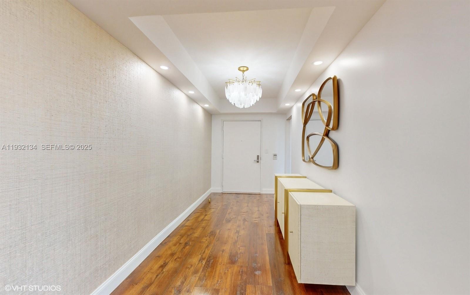 A hallway features wood flooring, a textured wall, a chandelier, and a modern console table — 10155 Collins Ave # 410, Bal Harbour FL 33154, BAL HARBOUR, FL