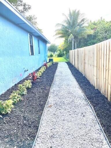 A gravel pathway runs between a blue house wall and a wooden privacy fence — 610 SE 2nd Avenue, Delray Beach FL 33483, DELRAY BEACH, FL