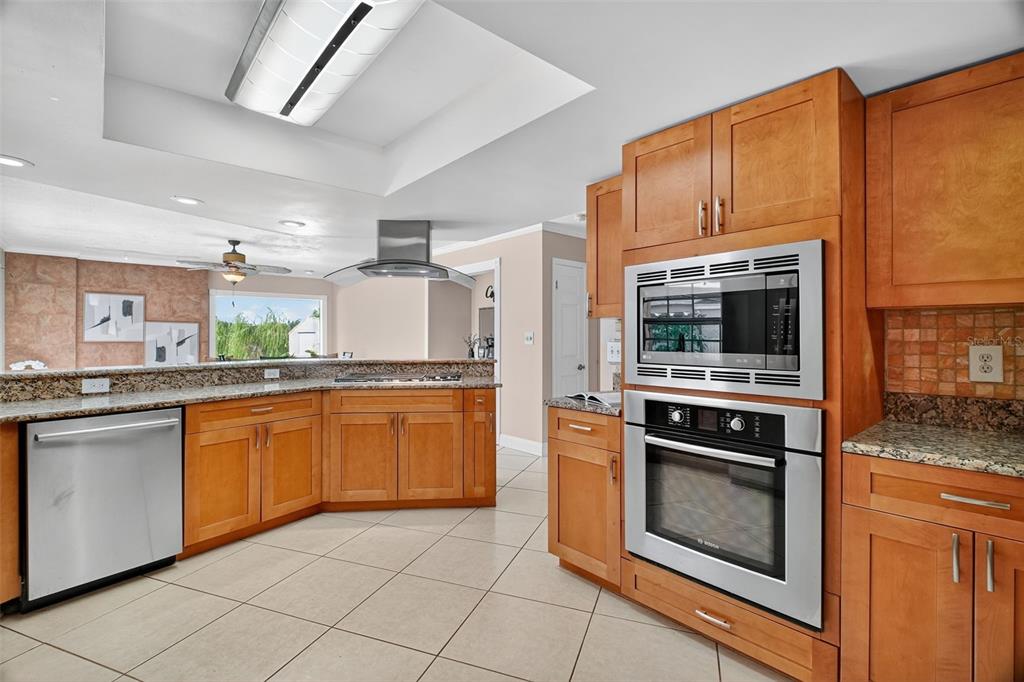 A kitchen features wood cabinets, stainless steel appliances, granite countertops, and light-colored tile flooring — 2514 TUSCARORA TRAIL, MAITLAND, FL