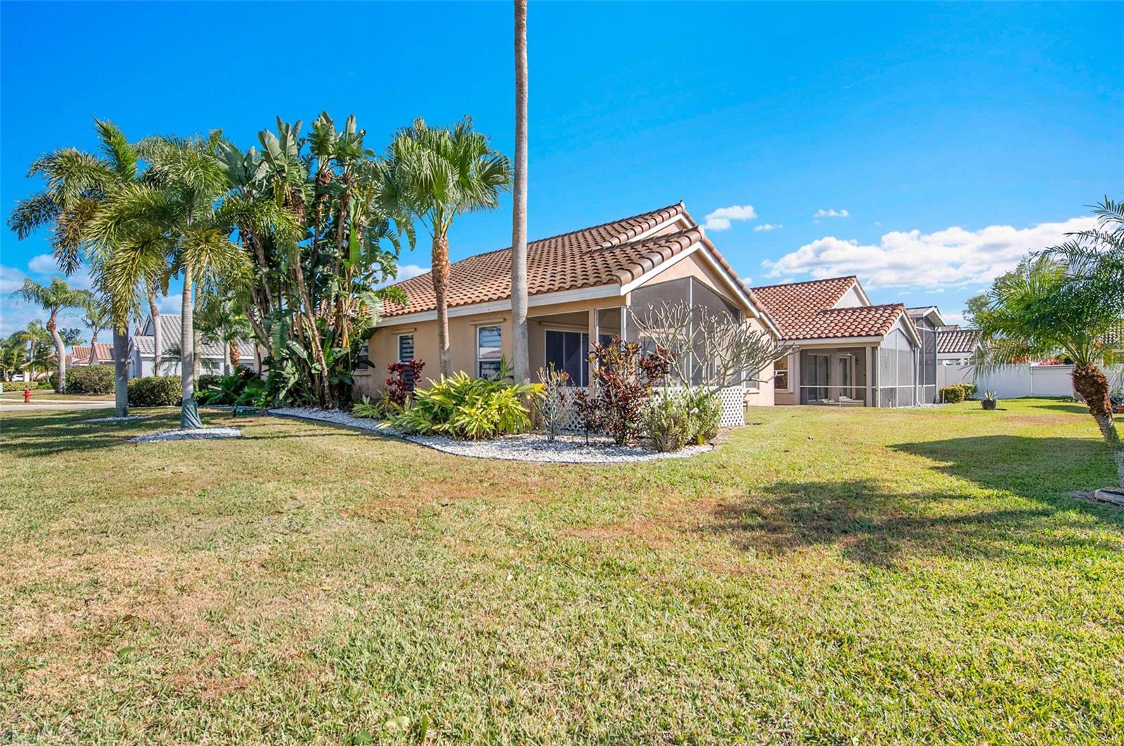A tan house with a tiled roof and a screened-in patio sits on a grassy lawn — 7491 Stirling Bridge Boulevard, Delray Beach FL 33446, DELRAY BEACH, FL