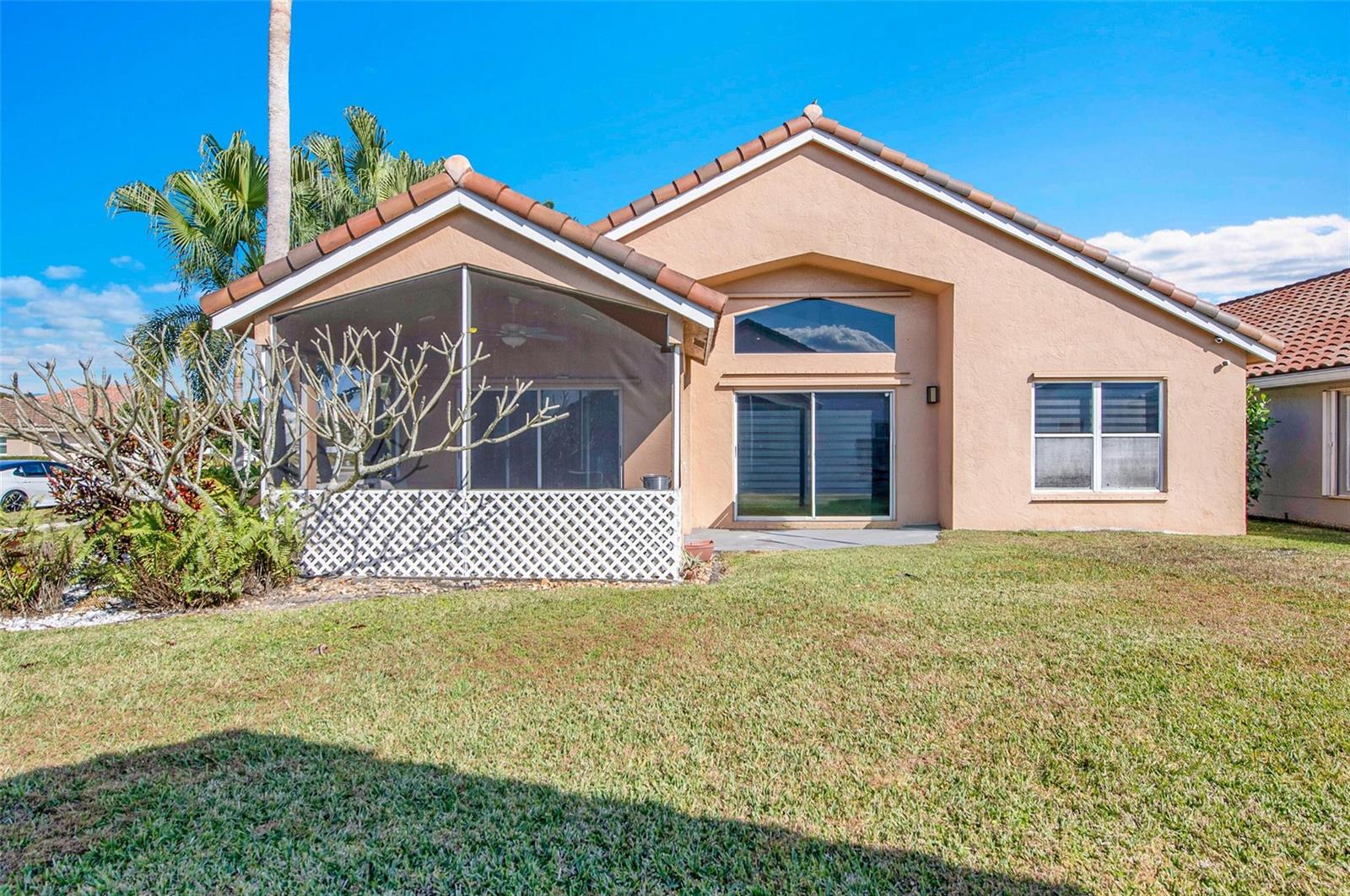 The rear exterior of a tan stucco house features a screened-in lanai and a lawn — 7491 Stirling Bridge Boulevard, Delray Beach FL 33446, DELRAY BEACH, FL