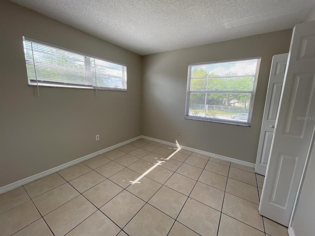 An empty bedroom features beige walls, light-colored tile flooring, and two windows with blinds — 722 W COLUMBIA AVENUE UNIT 722, KISSIMMEE, FL