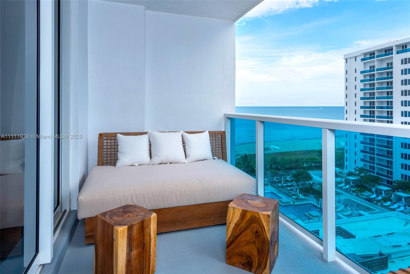 A balcony features a wooden daybed with white cushions and two wooden stump stools — 102 24th St # 1106, Miami Beach FL 33139, MIAMI BEACH, FL