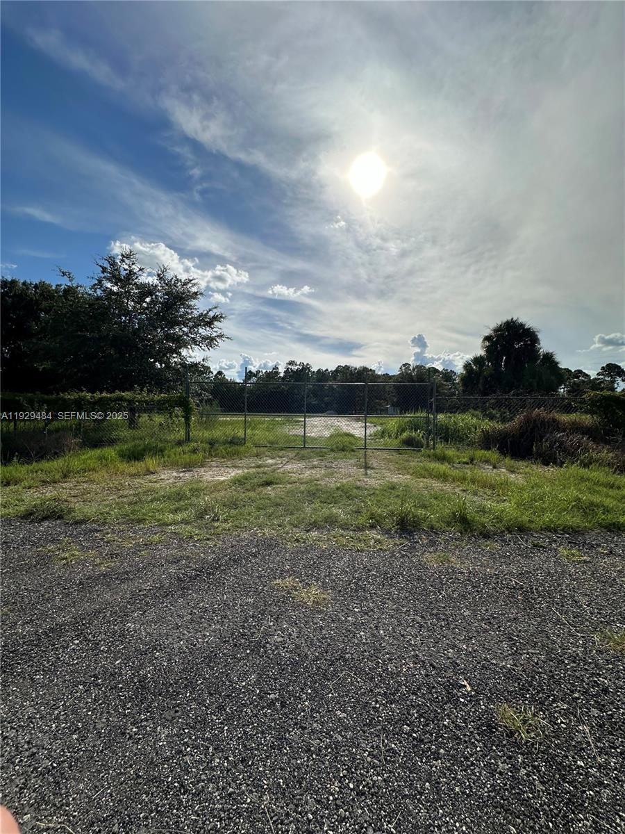 A gravel driveway leads to a chain-link gate opening onto a grassy, fenced lot — 420 S. CORAL ST., Clewiston FL 33440, CLEWISTON, FL