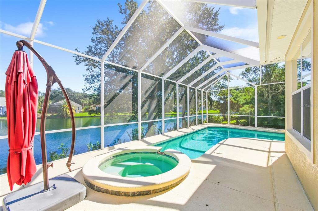 A screened-in patio features a swimming pool and a hot tub overlooking a lake — 17 SANDPIPER COURT, PALM COAST, FL