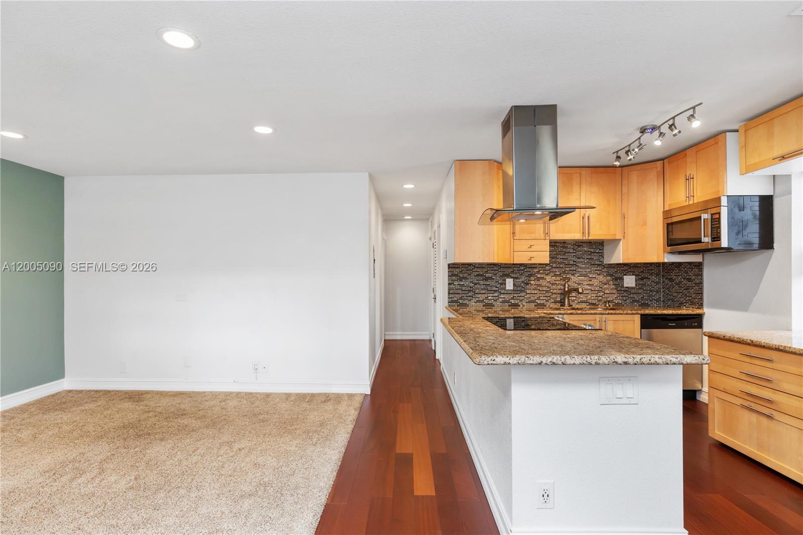 A kitchen with light wood cabinets and granite countertops overlooks a carpeted living area — 854 Normandy R # 854, Delray Beach FL 33484, DELRAY BEACH, FL
