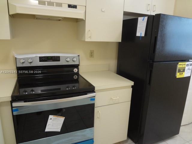 A kitchen features a black electric range and a matching black refrigerator with beige cabinets — 426 NE 210th Cir Ter # 2, Miami FL 33179, MIAMI, FL