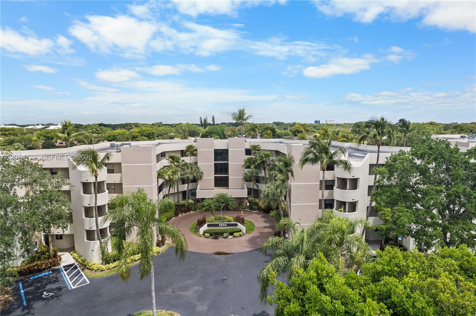 An aerial view shows a multi-story beige apartment building with a circular driveway and landscaping — 5850 Camino Del Sol # 404, Boca Raton FL 33433, BOCA RATON, FL