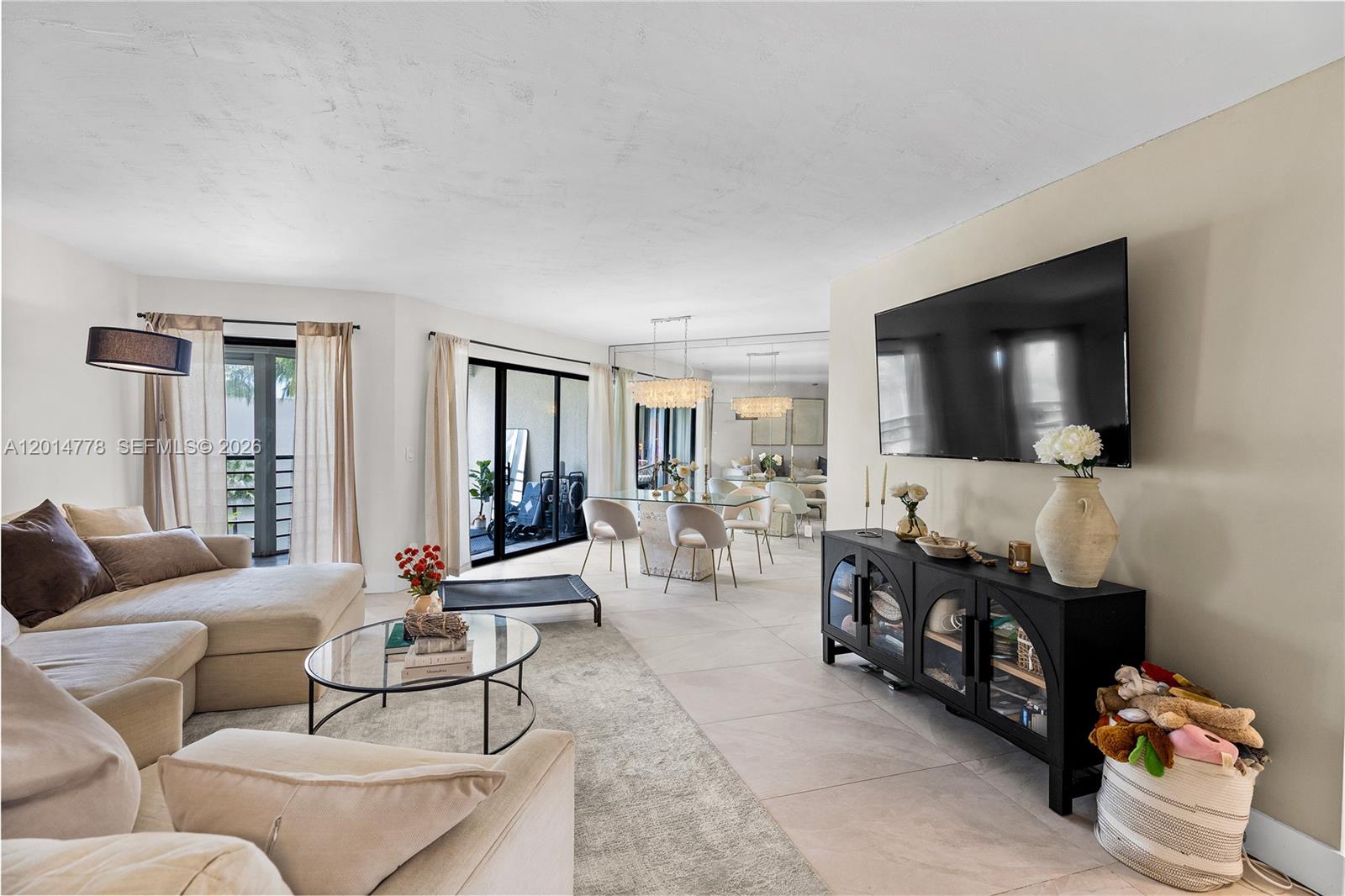 A living and dining area features tile floors, a wall-mounted television, and sliding glass doors — 5850 Camino Del Sol # 404, Boca Raton FL 33433, BOCA RATON, FL