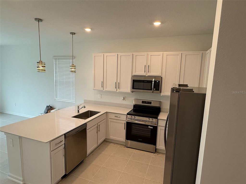 A kitchen features white cabinets, stainless steel appliances, and a quartz-topped island with a sink — 2691 SKYLINE LOOP, KISSIMMEE, FL