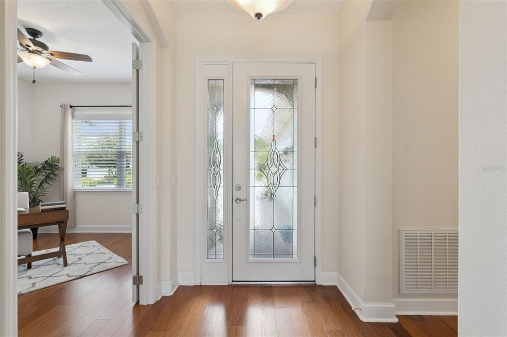 An entryway features a white front door with decorative glass, hardwood floors, and an adjacent room — 1121 GARDENSHIRE LANE, DELAND, FL