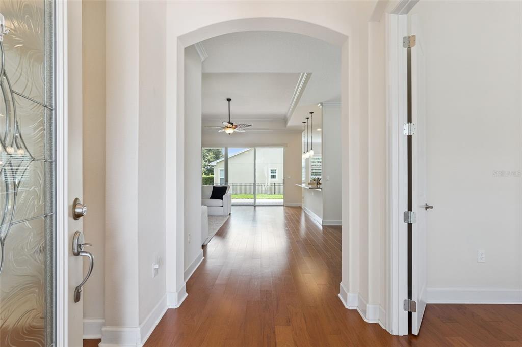 A view through an arched entryway into a bright living area with hardwood floors — 1121 GARDENSHIRE LANE, DELAND, FL