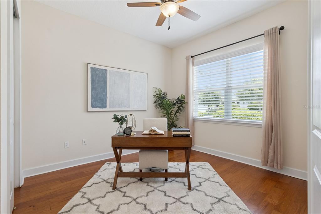 A home office features a wooden desk, a patterned rug, and a window with curtains — 1121 GARDENSHIRE LANE, DELAND, FL