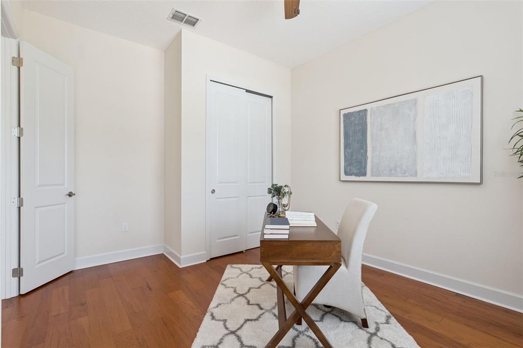 A home office features hardwood floors, a wooden desk, a white chair, and wall art — 1121 GARDENSHIRE LANE, DELAND, FL